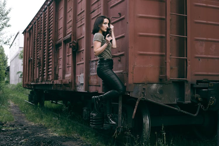 A Woman Holding A Gun While Hanging On A Cargo Train