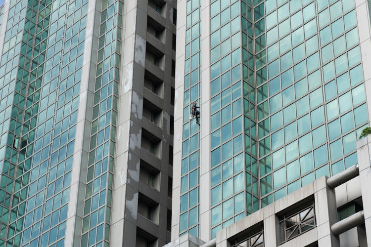 A Person Cleaning Windows Of A Building Hanging On A Rope