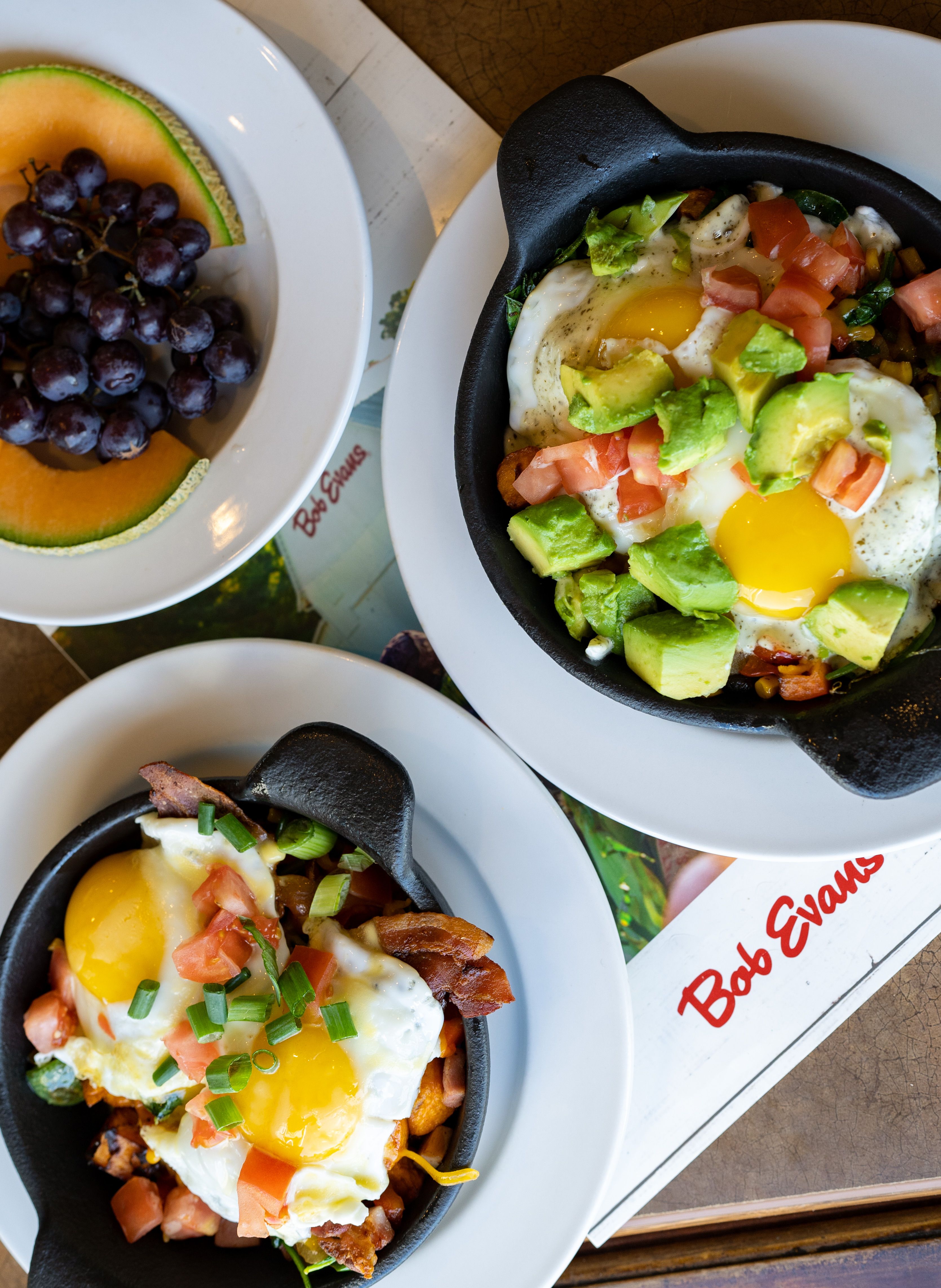 A top view of a breakfast skillet with eggs, avocado, and a side of fruit.