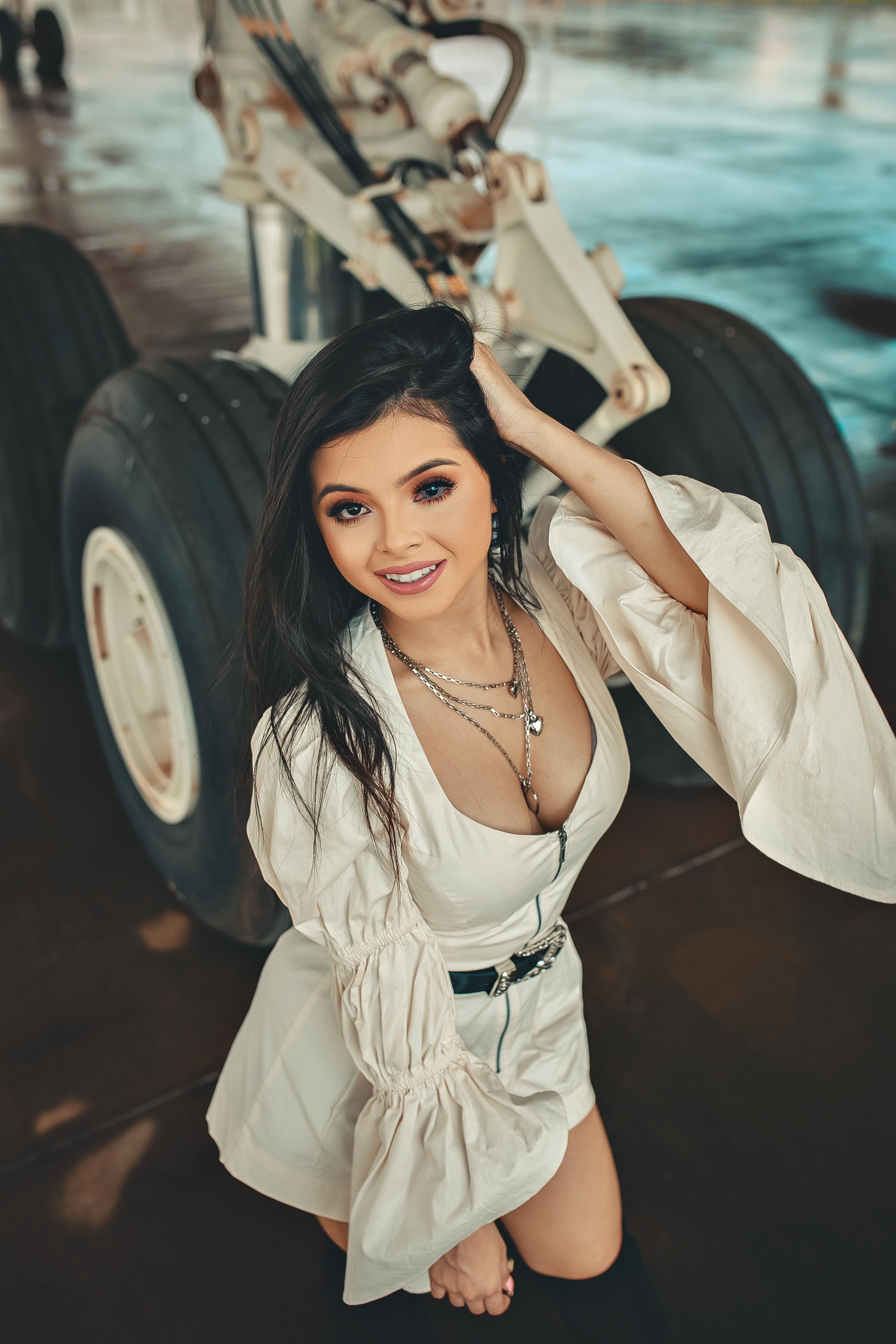 Stylish model in a beige dress poses near aircraft wheels at an airport.