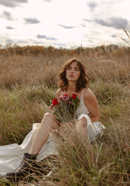 Free A young woman holding a bouquet of flowers, sitting in a meadow during summer. Stock Photo