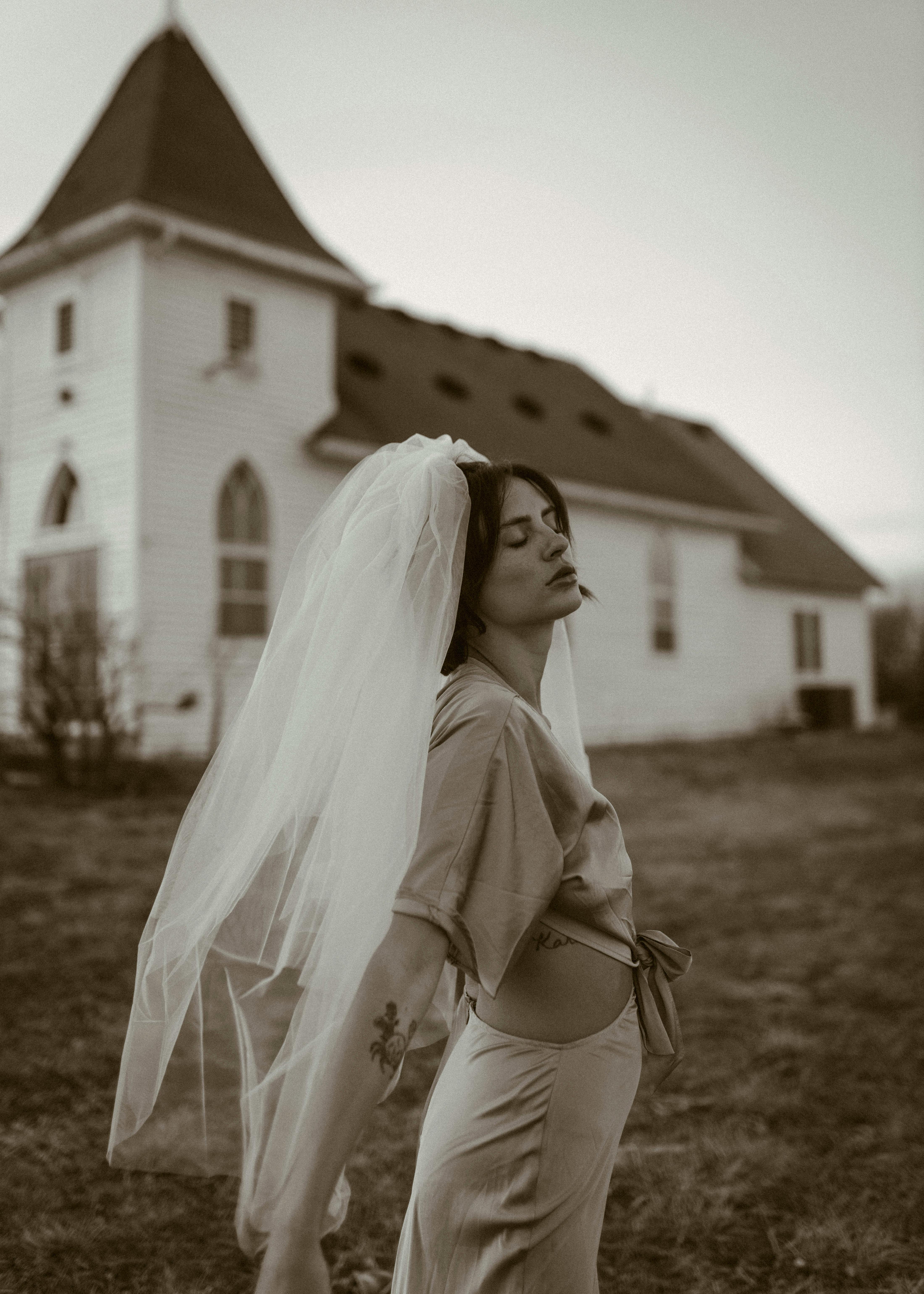 一位穿着复古连衣裙、戴着面纱的宁静新娘在得梅因的一座乡村教堂外摆姿势