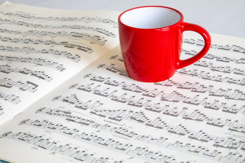 A vibrant red mug placed on an open sheet music, creating a harmonious still life composition.