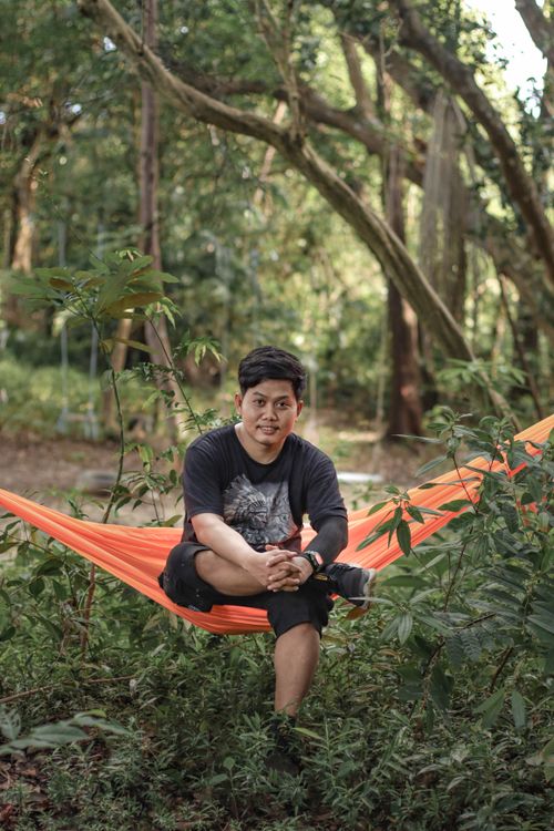 Free A man relaxes on an orange hammock in a lush forest, enjoying the tranquil surroundings. Stock Photo