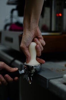 Close-up of a barista using a tamper on coffee grounds at a cafe, highlighting precision and craft.