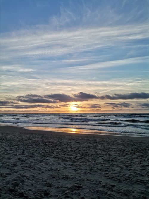 Free Beautiful sunset over a beach in Lithuania with golden hues reflecting on the waves. Stock Photo