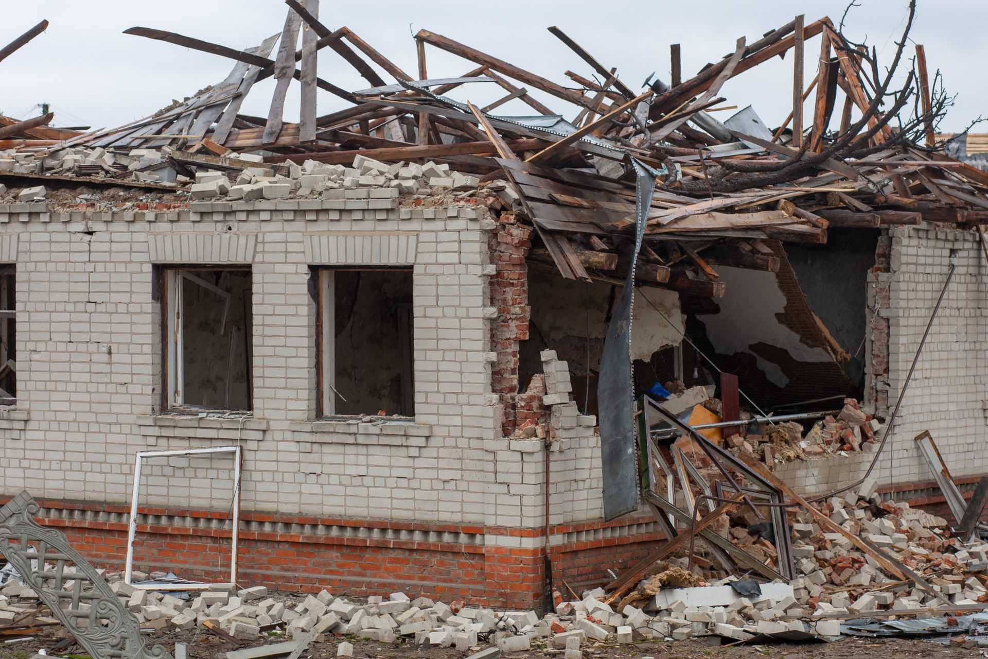 A collapsed brick house showing severe structural damage with debris and broken wooden beams.