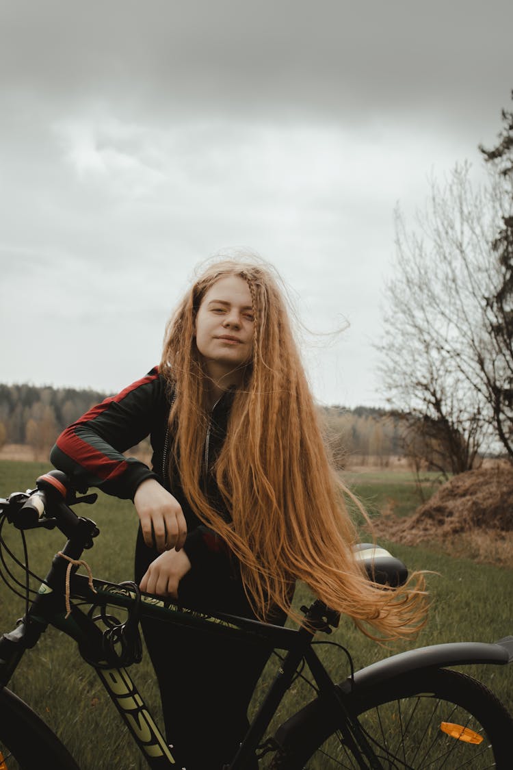 Girl With Long Hair Leaning On A Bike On A Field