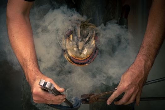 A blacksmith skillfully forges a horseshoe, surrounded by smoke, showcasing traditional craftsmanship.