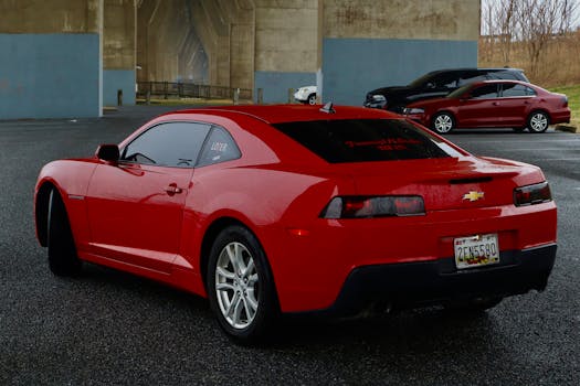 Rear view of a red Chevrolet Camaro parked outdoors on wet pavement.