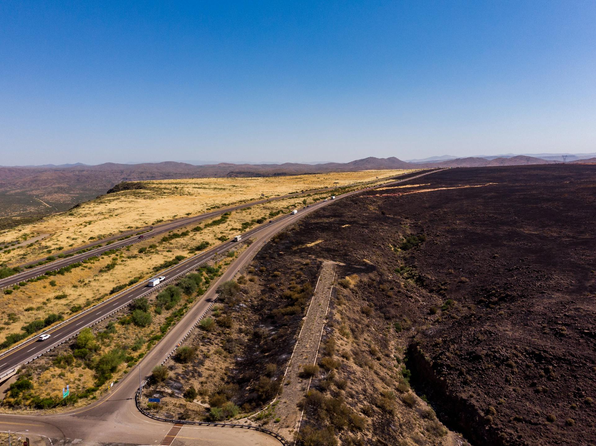 Aerial view of an Arizona highway amid arid and burned landscape showing stark contrasts.