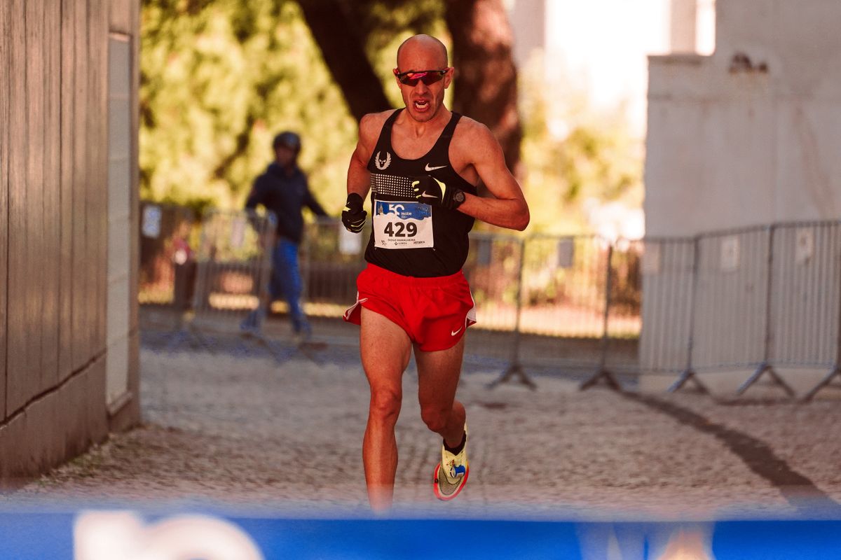 Male runner mid-stride during a road race, showing a compact stride with the foot landing close under the body