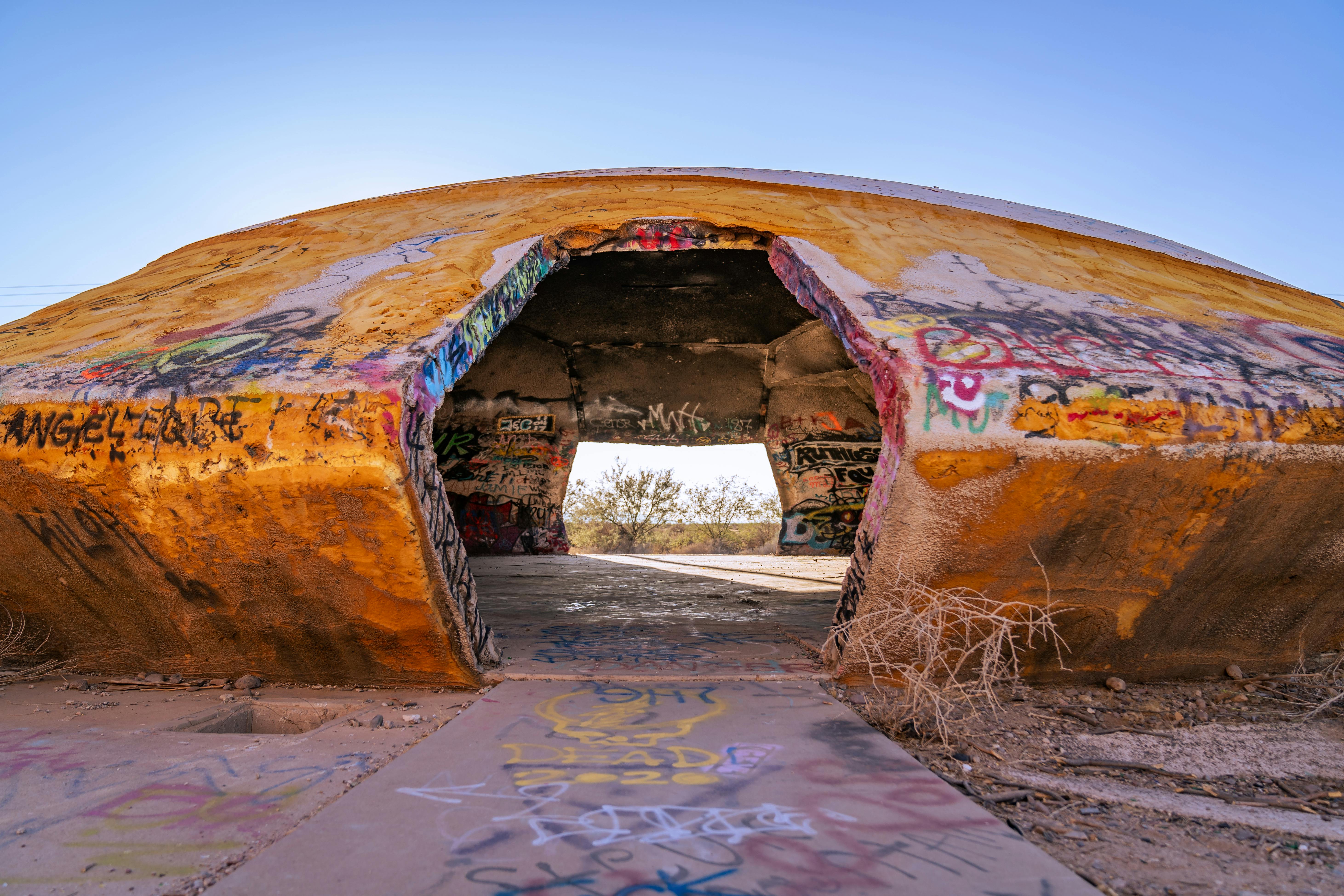 An abandoned dome structure featuring colorful graffiti and signs of vandalism in a desert setting.