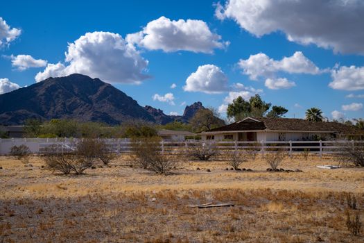 Charming rural farmhouse set against Arizona's stunning mountain scenery, under a bright blue sky.