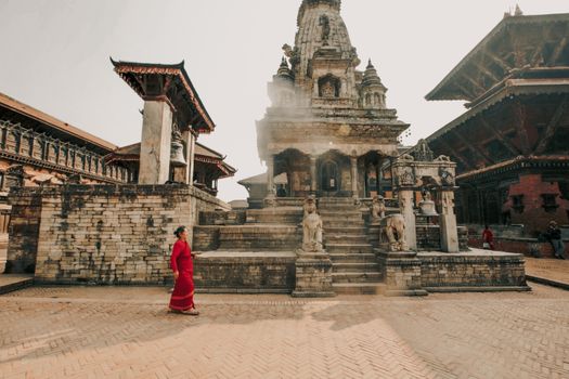 A woman in a red sari walks past ancient architecture at Bhaktapur Durbar Square, a UNESCO World Heritage Site in Nepal.