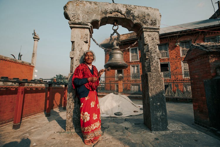 Elderly Hindu Woman Ringing Bell Of Ancient Arch