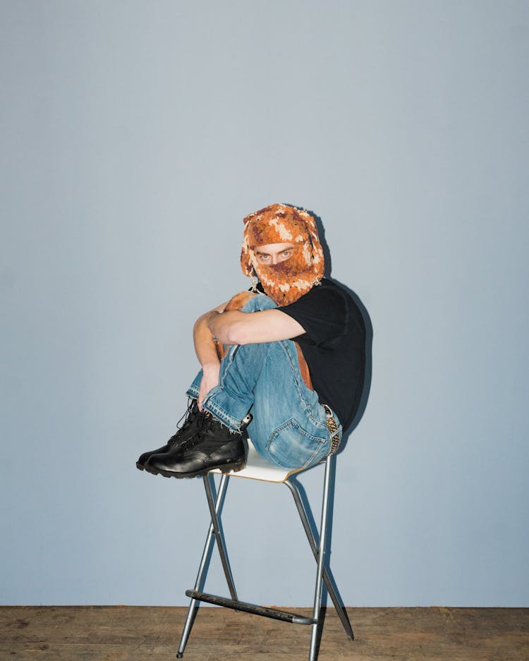 Man Sitting On A Stool With His Face Covered In A Cloth 