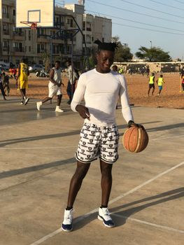 A young man dribbling a basketball on an outdoor court in a city environment.