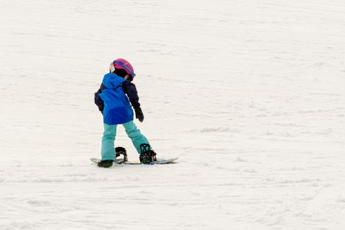 Free Young child learning to snowboard on a winter day, with ample snow and bright gear. Stock Photo