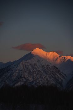 Sunrise illuminates a snow-capped mountain, creating a dramatic scene.