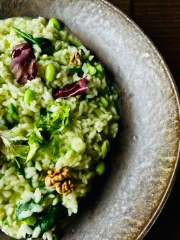 A close-up shot of green risotto garnished with fresh herbs and walnuts.