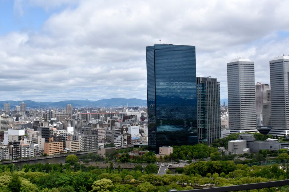 Urban skyline with modern skyscrapers surrounded by greenery under a cloudy sky.