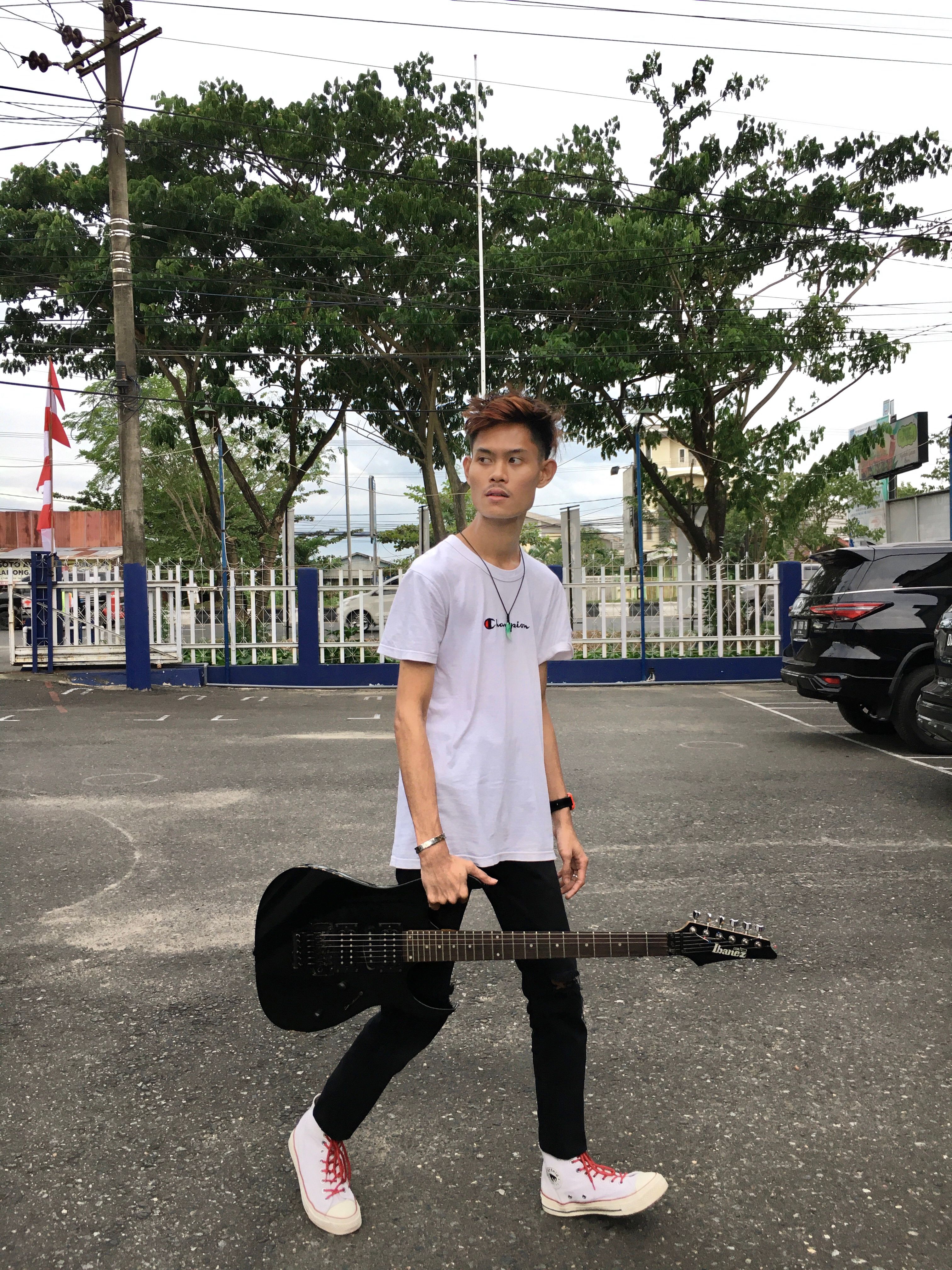 A teenage musician holds an electric guitar in an outdoor setting in South Kalimantan, Indonesia.