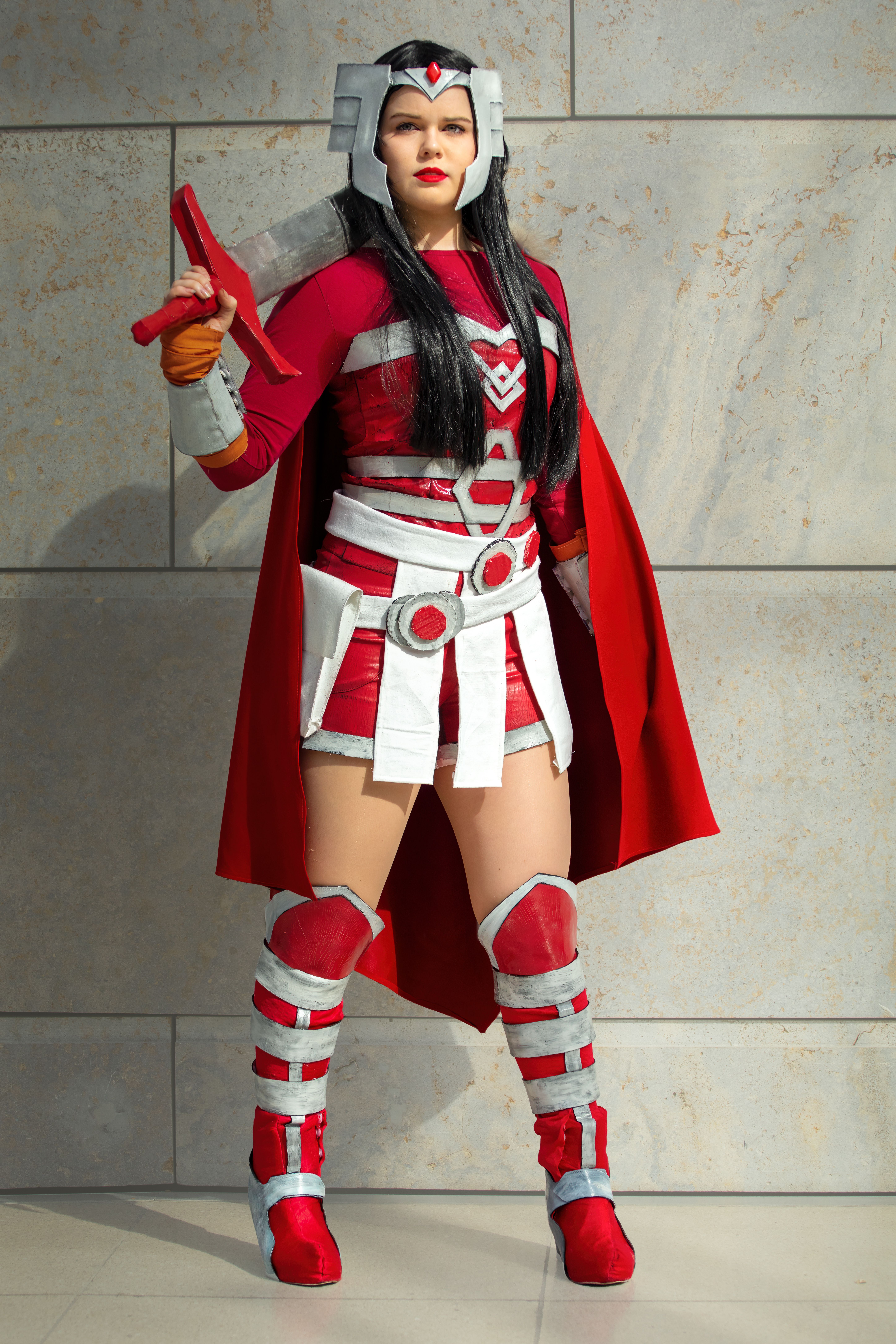 A woman in a vibrant red and white cosplay costume posing indoors. Full body shot.