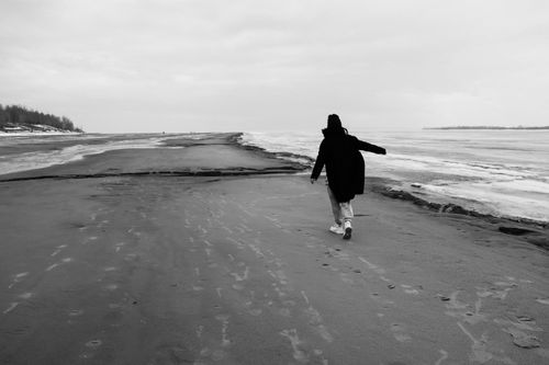 Free A person walks along a desolate beach in black and white during winter. Serene and contemplative scenery. Stock Photo