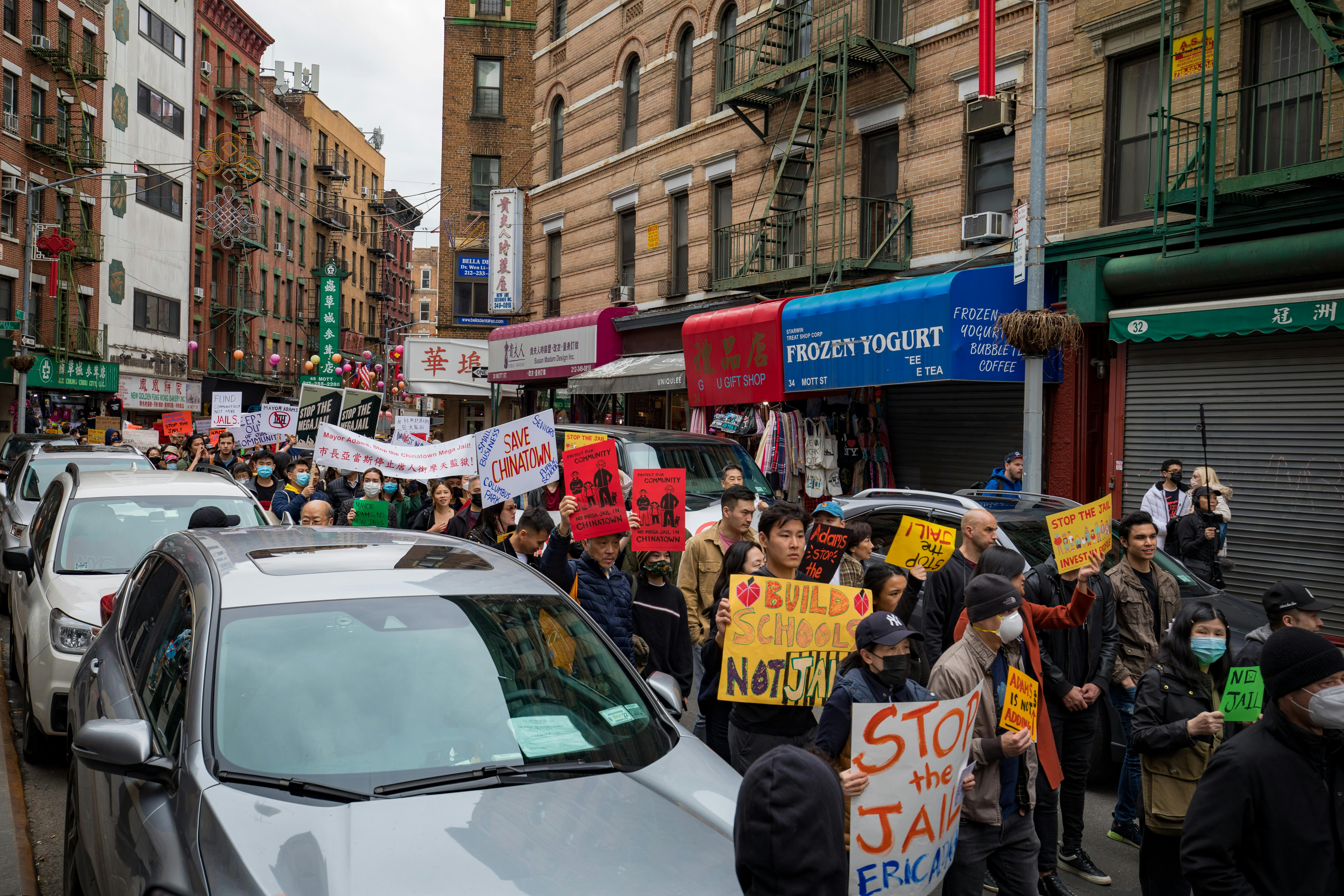 Protestors gather in New York City's Chinatown advocating for community issues with vibrant signs.