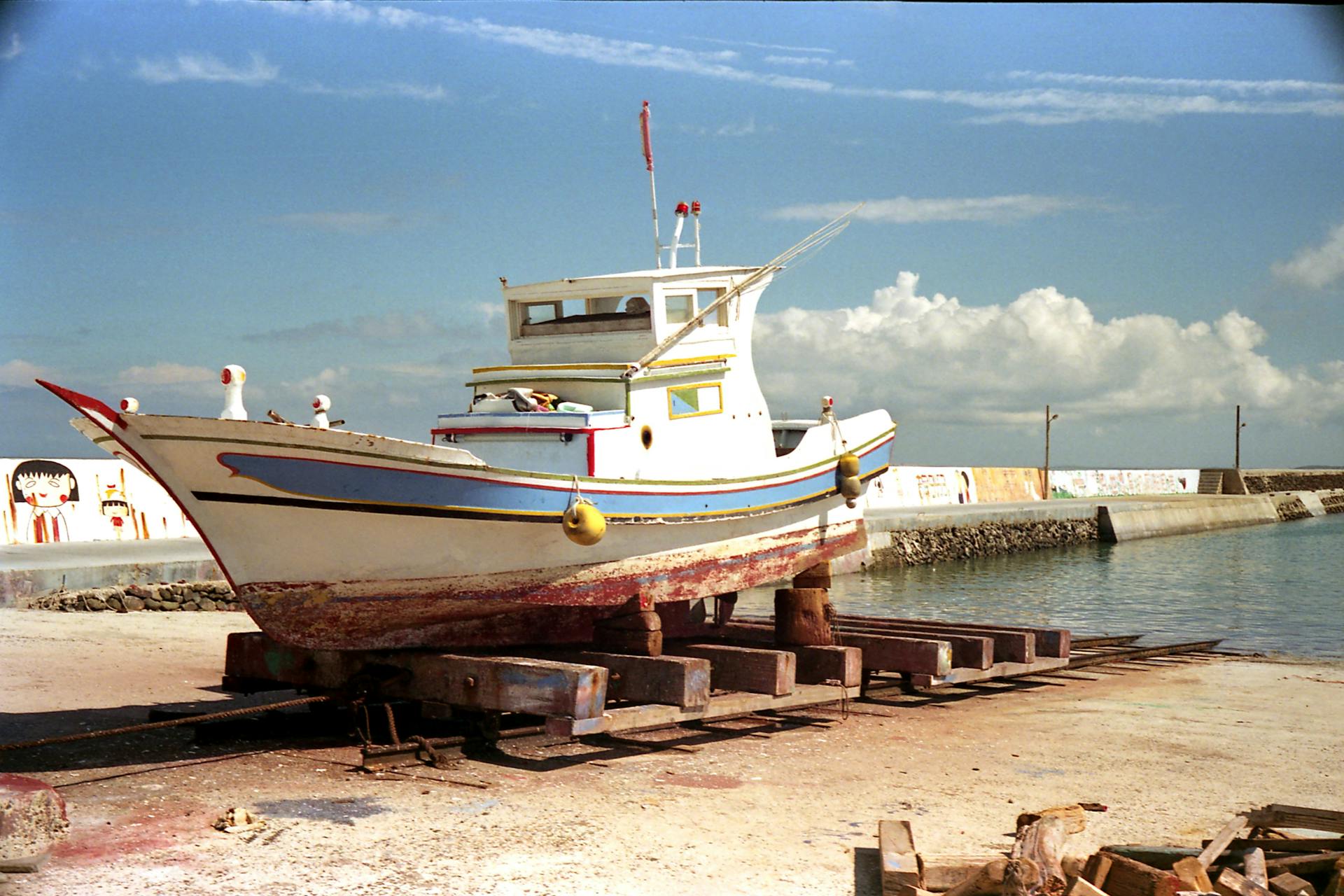 An abandoned fishing boat on a dry dock at a harbor in Taiwan with a clear blue sky.
