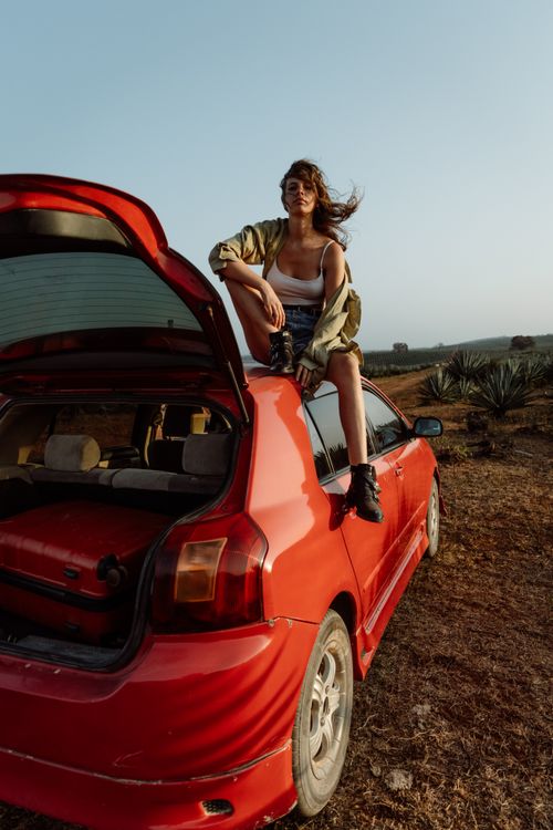 Free Stylish woman atop red car in rural setting, enjoying an adventure. Stock Photo