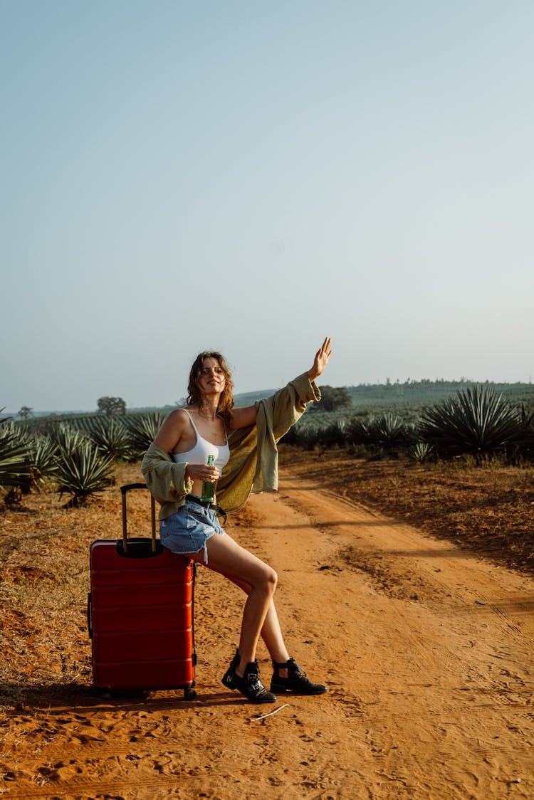 Woman Seated On A Red Suitcase Doing A Hitchhike 