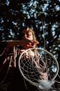 Artistic shot of a woman holding a dreamcatcher in a sunlit forest setting.