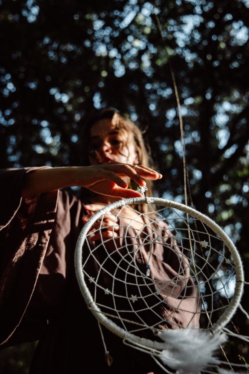 Free Artistic shot of a woman holding a dreamcatcher in a sunlit forest setting. Stock Photo
