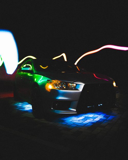 Free A sleek car illuminated by colorful light trails and reflections at night, creating a vibrant scene. Stock Photo