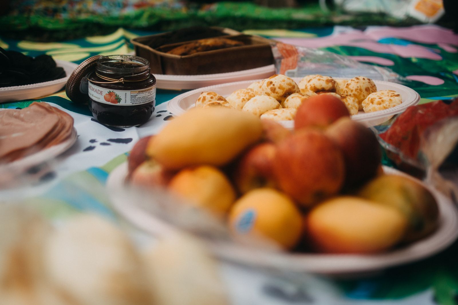 A colorful picnic spread featuring fruits, jam, and assorted pastries on a vibrant tablecloth.