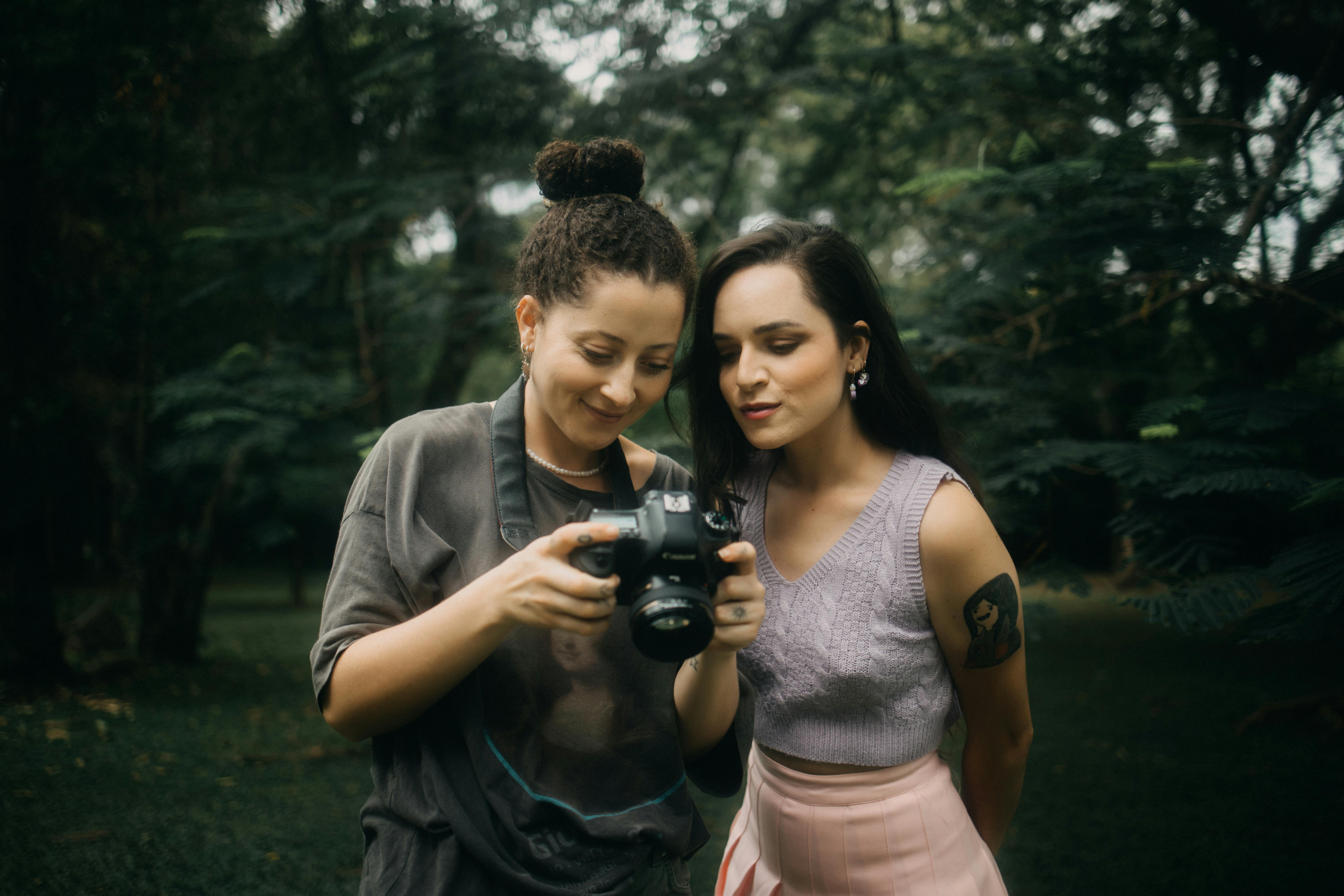 Two women in a park reviewing photos on a digital camera, enjoying outdoor photography.