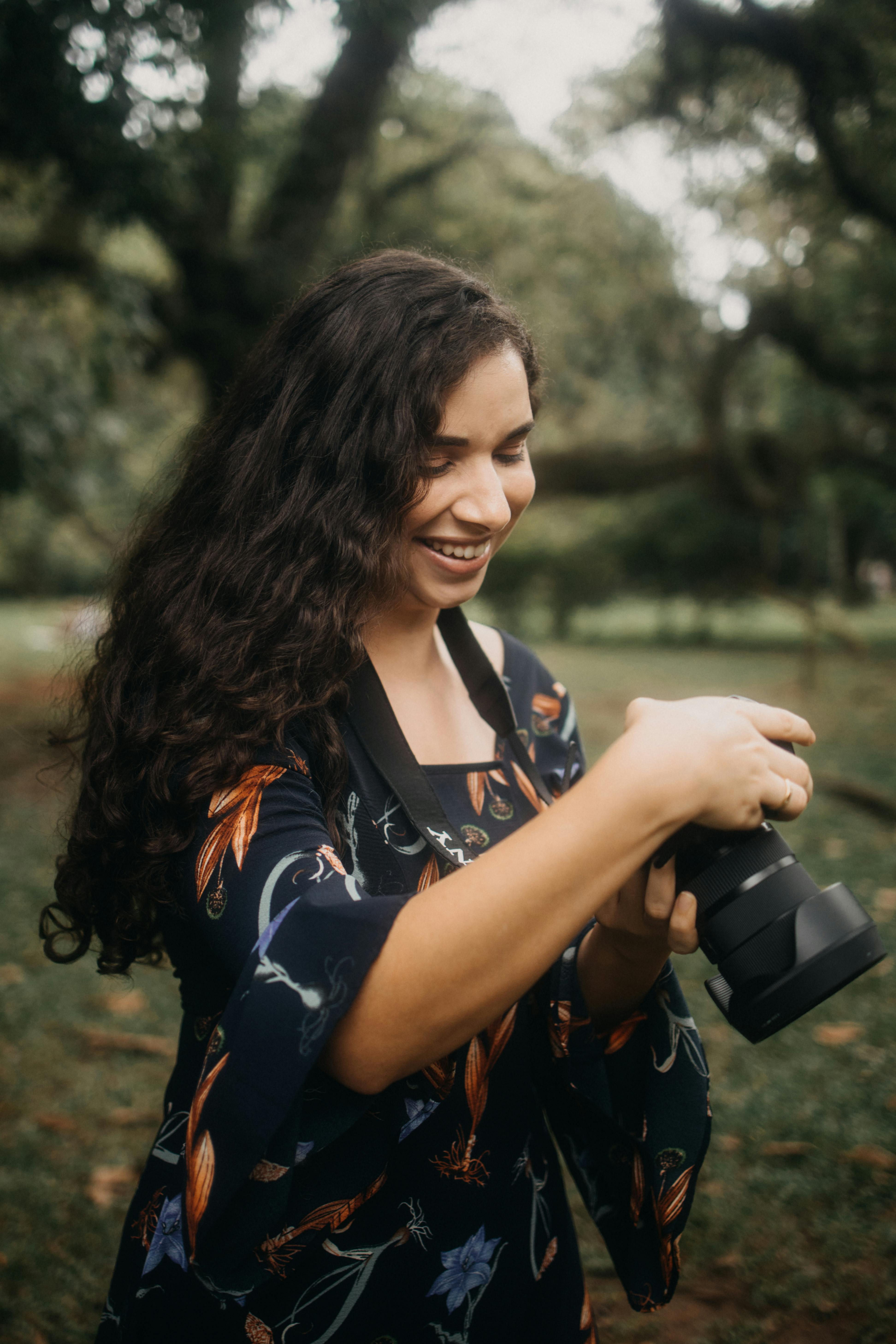 Portrait of a woman photographer smiling while adjusting her camera in a park setting.