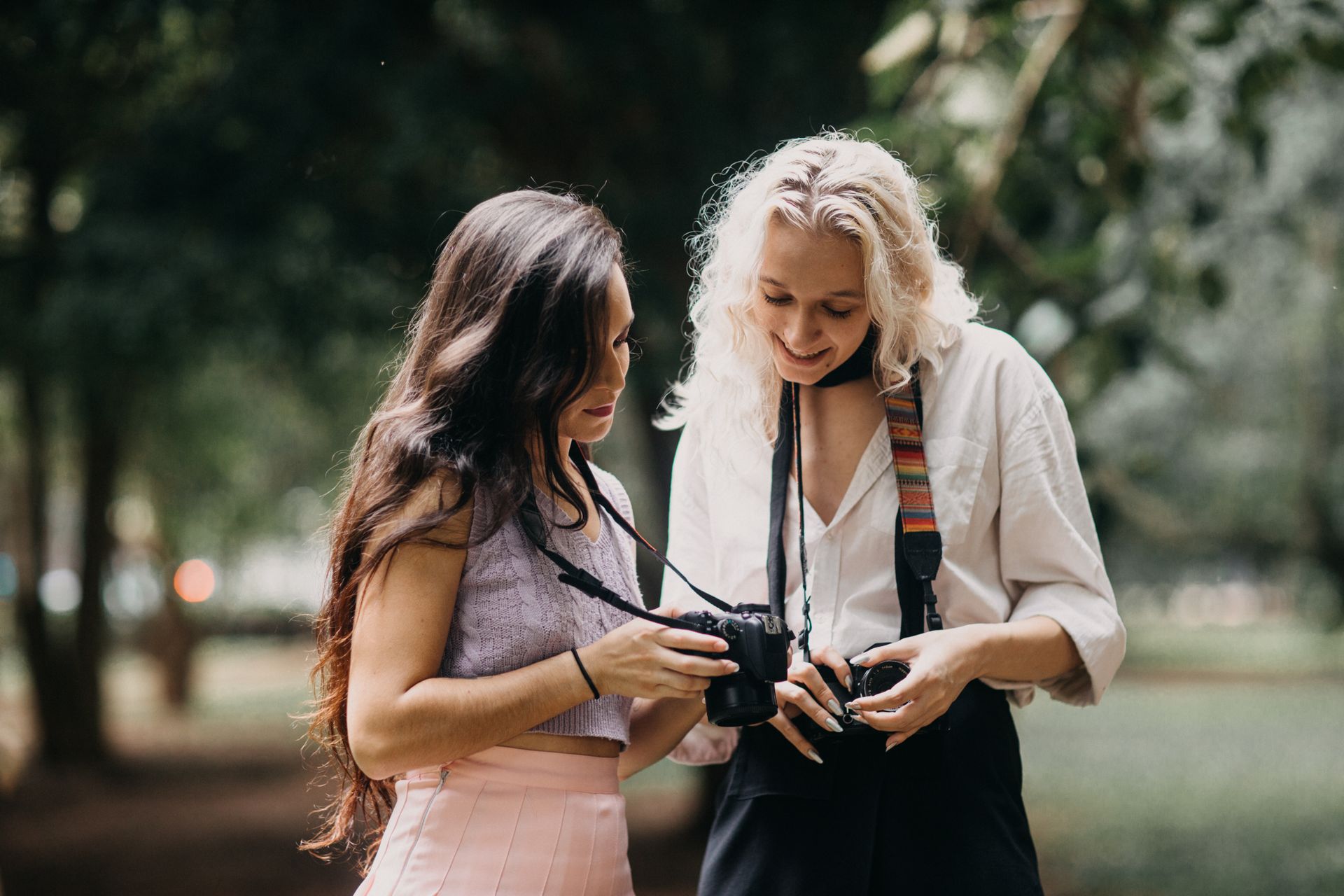 Two women enjoying photography together, sharing tips with cameras in a lush park setting.