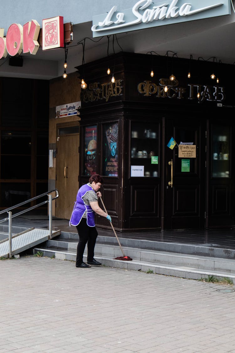 A Woman Mopping The Steps Outside A Building