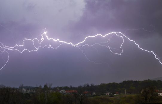 Vivid lightning bolts illuminate a dark, stormy sky over a rural area.
