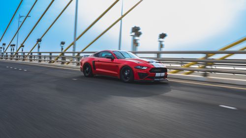 Free Dynamic shot of a red sports car speeding on a bridge in Kuwait with a clear blue sky. Stock Photo