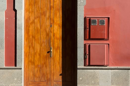 Minimalist capture of a wooden door set against a pink facade with utility boxes.