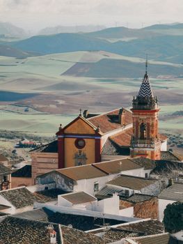Charming aerial shot of Cañete la Real, highlighting Iglesia de San Sebastián amid rolling fields and hills.