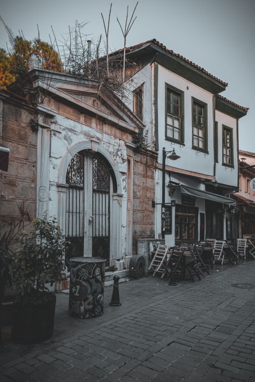 Free Rustic old building facade with empty outdoor seating on a quiet cobblestone street. Stock Photo