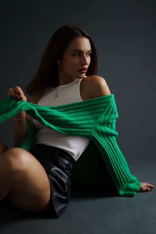 Woman wearing a bottle green funnel-neck sweater with a leather skirt