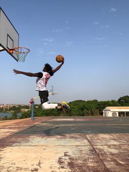 Dynamic shot of a black male athlete performing a mid-air dunk on a basketball court in Conakry, Guinea.