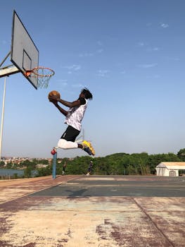 Athlete leaping for a basketball dunk outdoors on a sunny day.