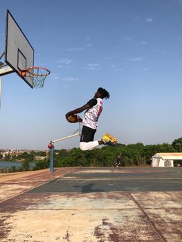 Athletic man performing an impressive basketball dunk on an outdoor court against a blue sky.